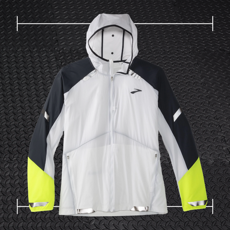 a white and black brooks running jacket with green accents laid on top a photo of black rubber gym flooring