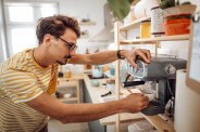 young casually clothed man making coffee in his domestic kitchen