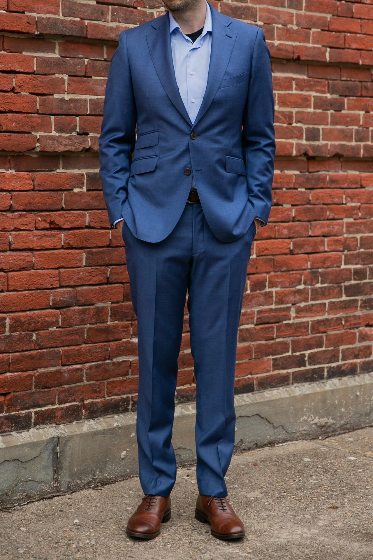 man in blue suit and brown shoes in front of brick wall