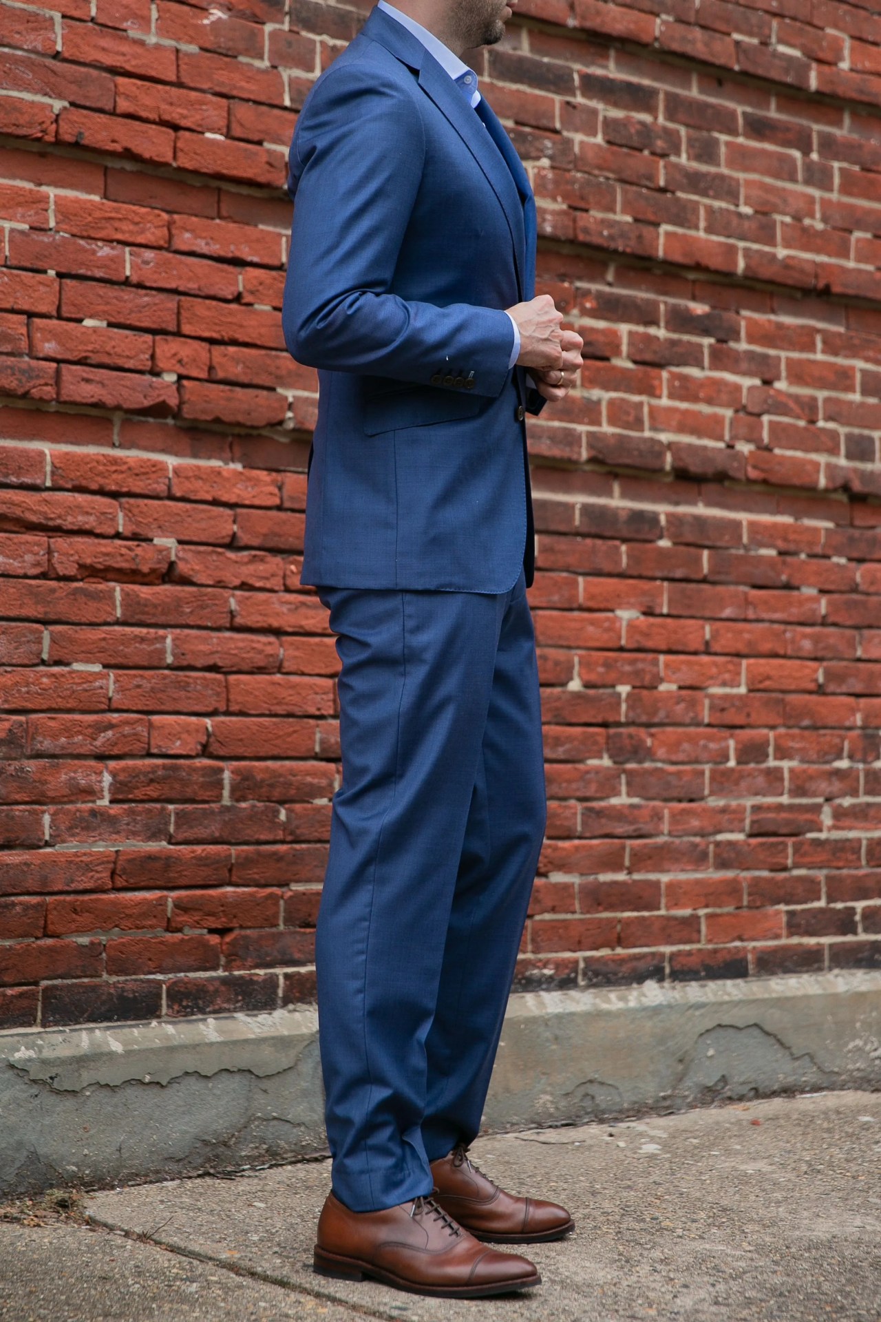 the side of a man wearing a custom blue suit in front of a brick wall