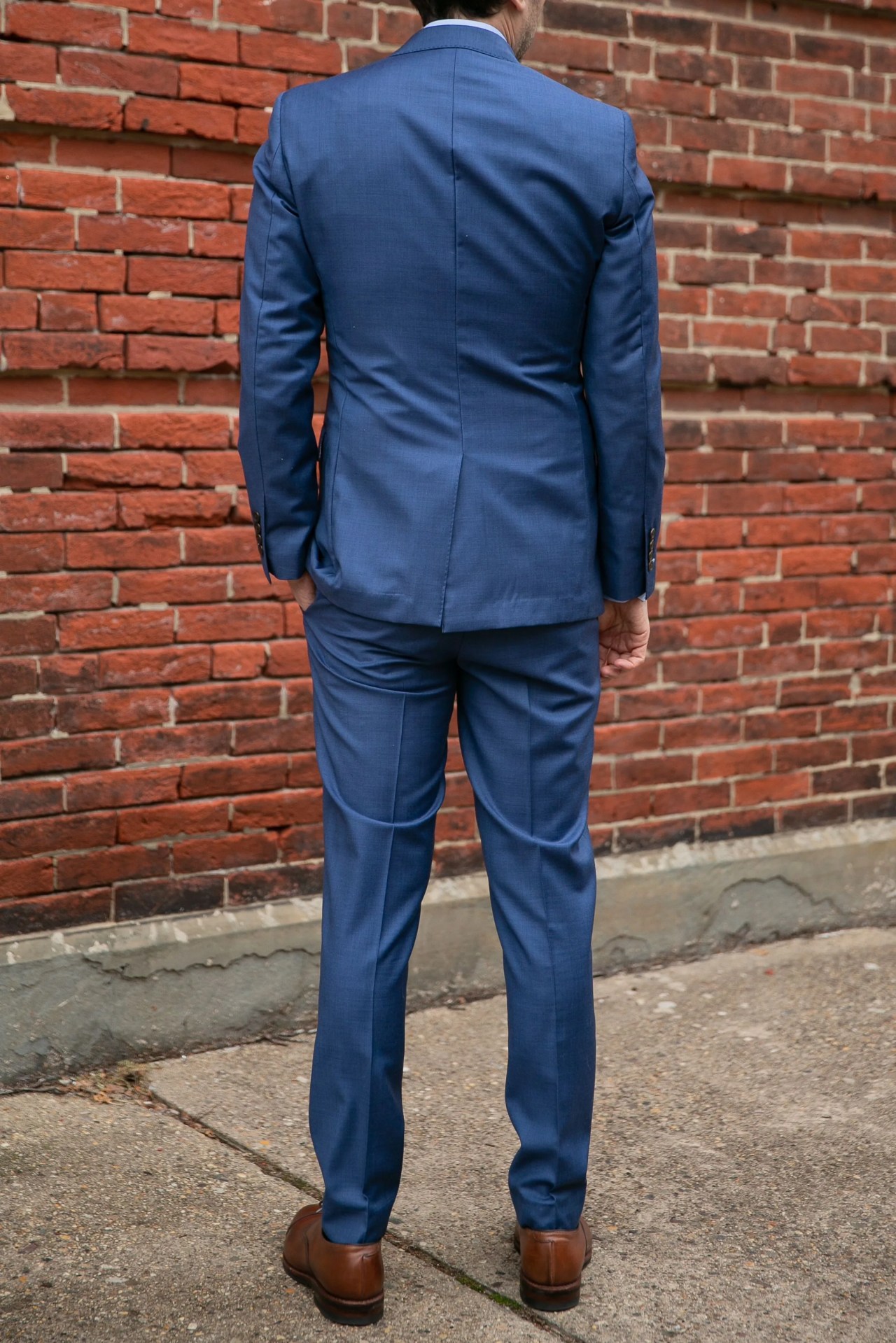 a man wearing a custom blue suit in front of a brick wall
