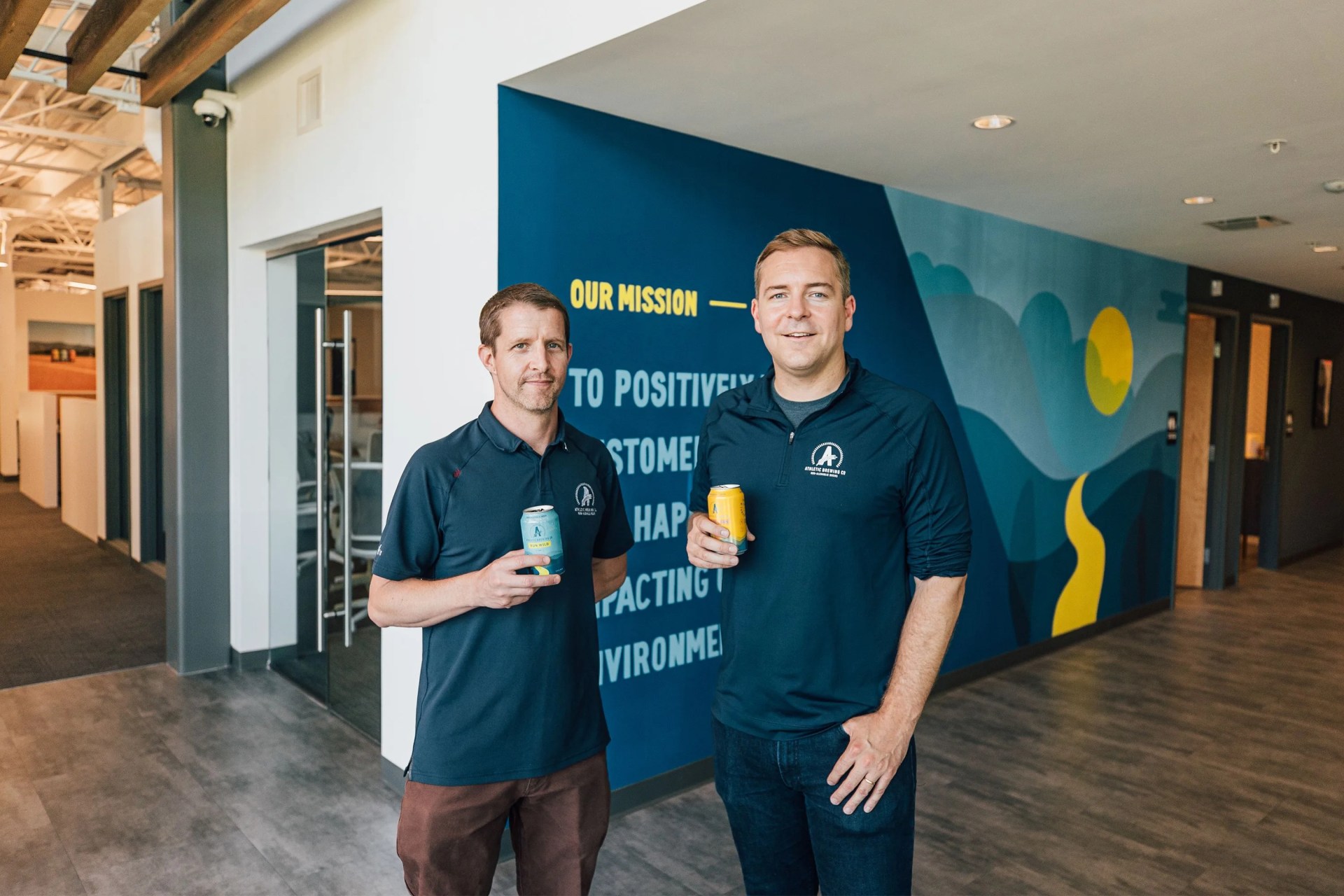 the two founders of athletic brewing holding cans of non alcoholic beer