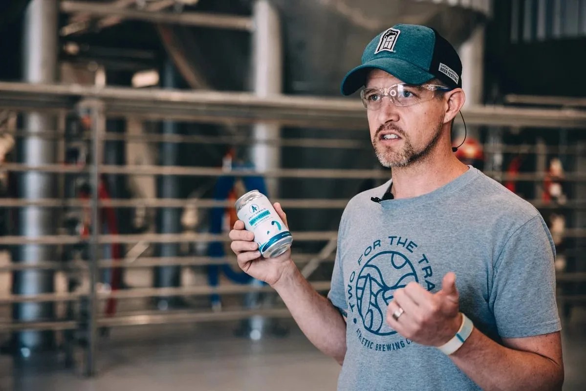 the co founder of athletic brewing company holding a beer and talking in the brewing