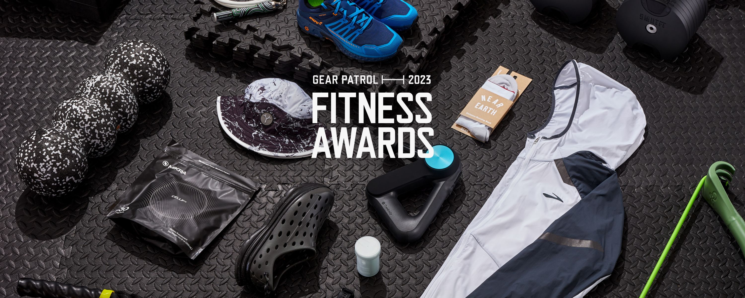 multiple pieces of fitness gear knolled out on top of black rubber gym flooring with text saying 2023 gear patrol fitness awards over top the photo
