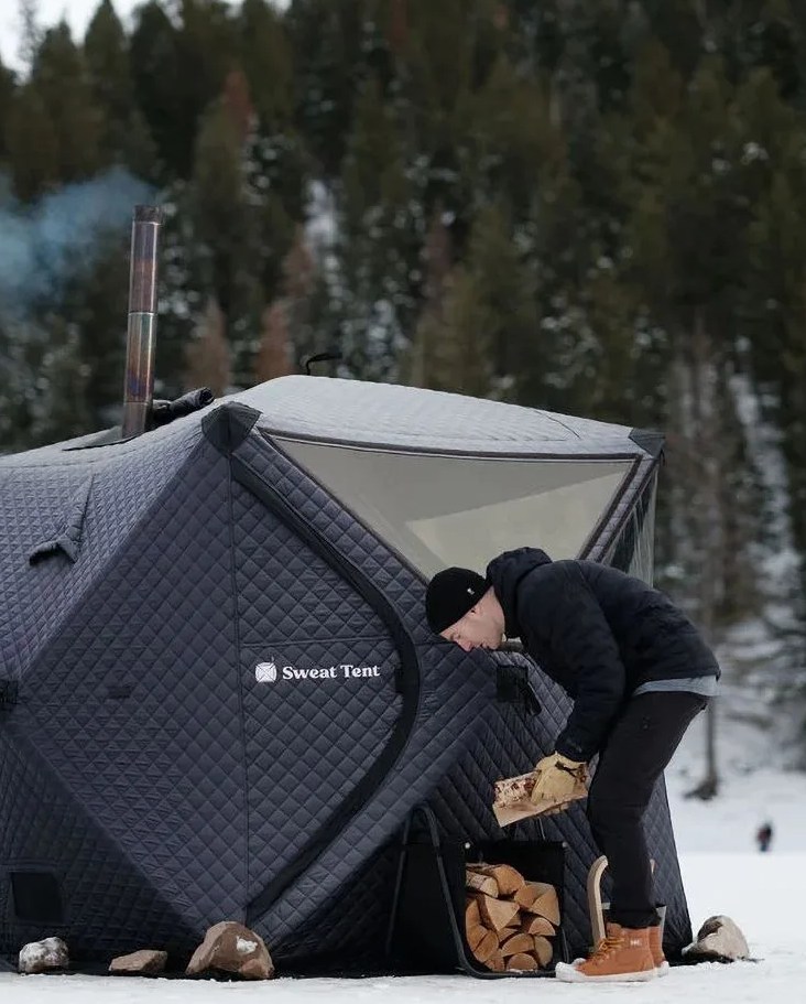 man setting up wood for his sweat tent sauna set up in a snowy area