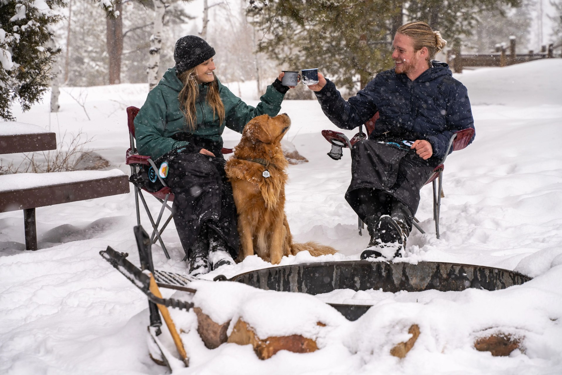 two people clinking cups sitting wearing mozy blanket with a dog