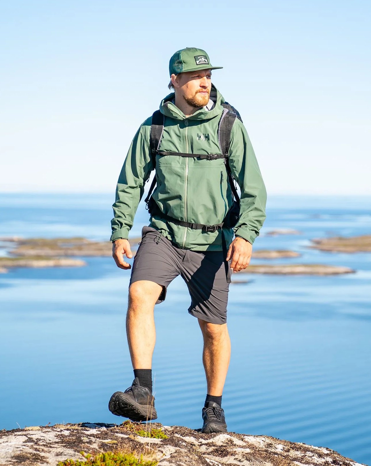 man wearing helly hansen ss23 new collection walking on rock overlooking ocean