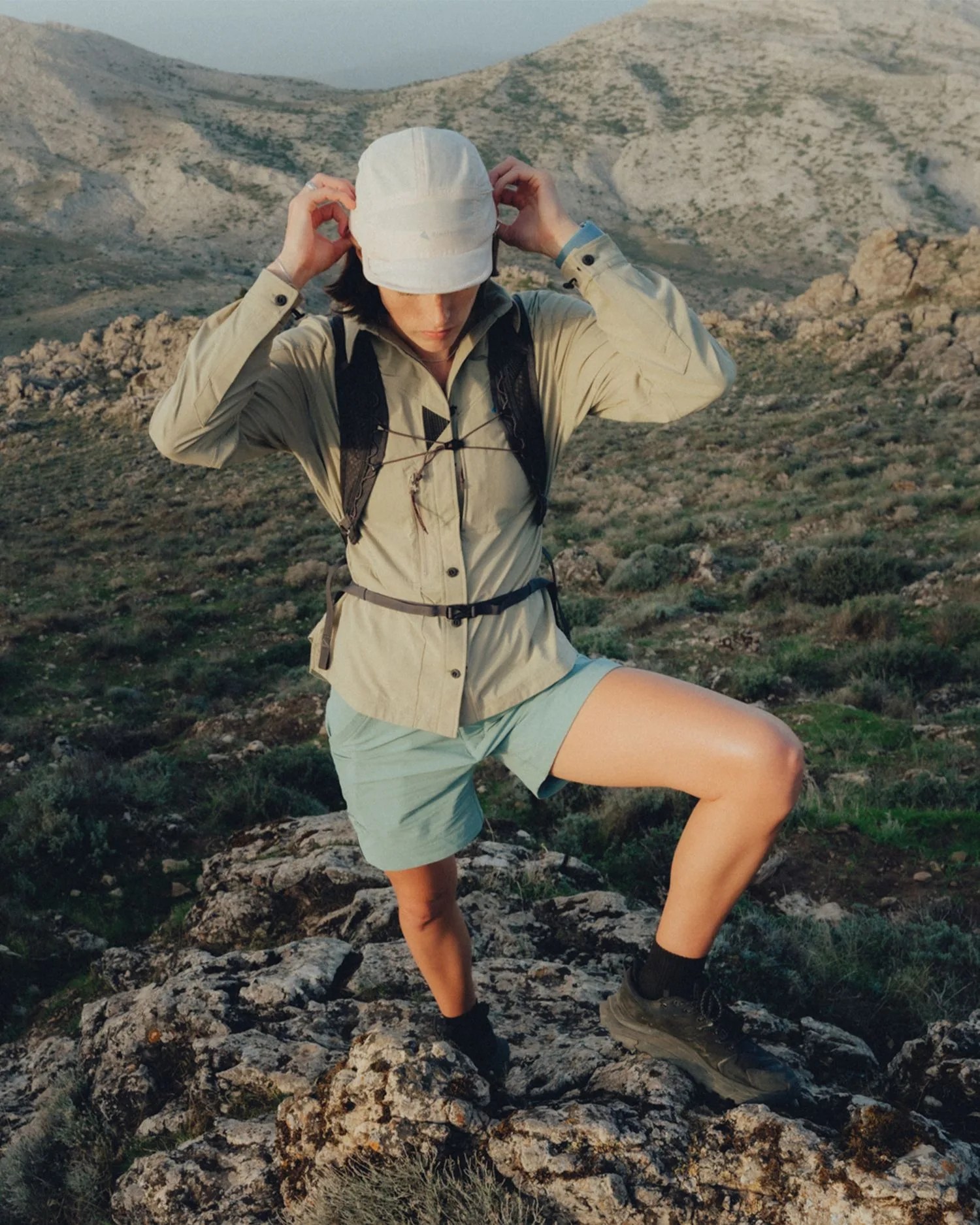 a person on a mountain wearing a hat, jacket, and shorts