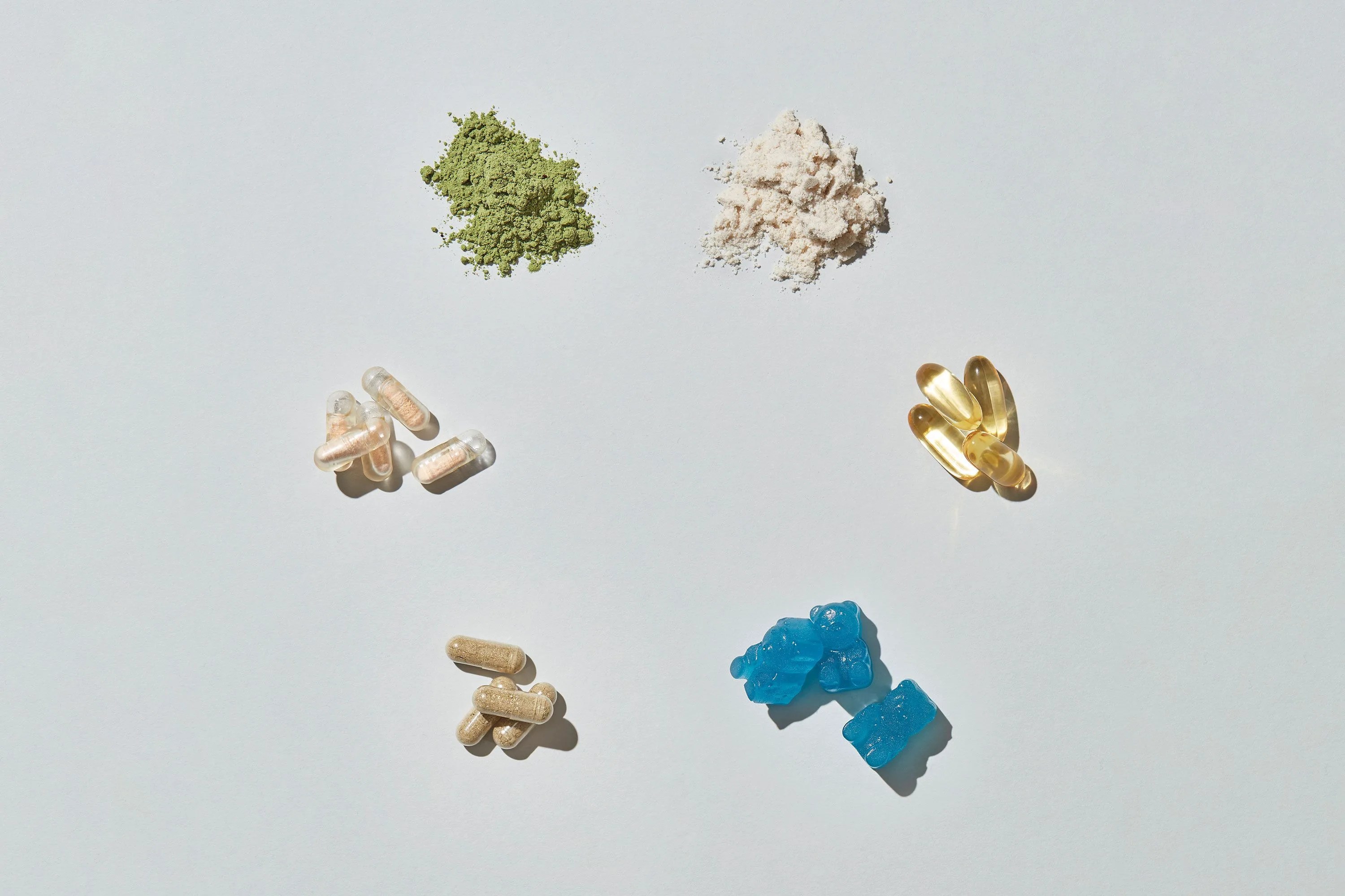 multiple pills, powders and supplements organized in a circle on a grey background