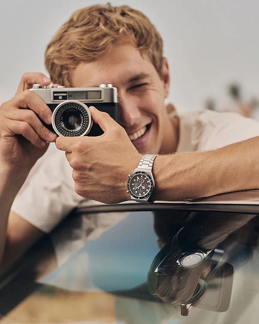 man taking a picture while wearing q timex three time zone chronograph 40mm stainless steel bracelet watch
