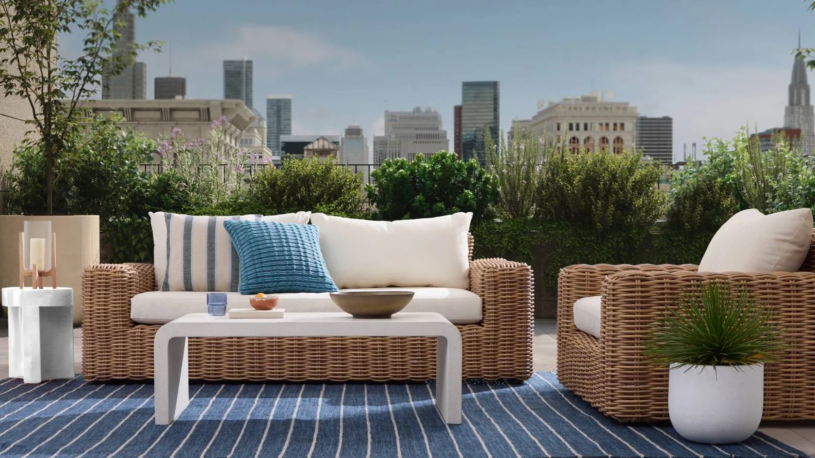 Wicker couch and chair surrounding coffee table on outdoor balcony with cityscape in background