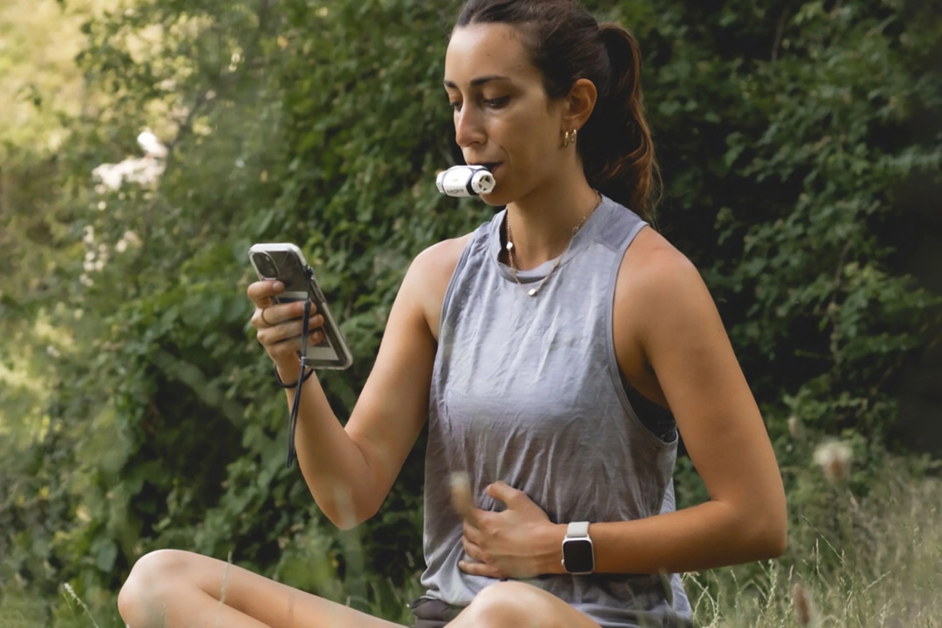 a woman sitting in a field using an airofit device