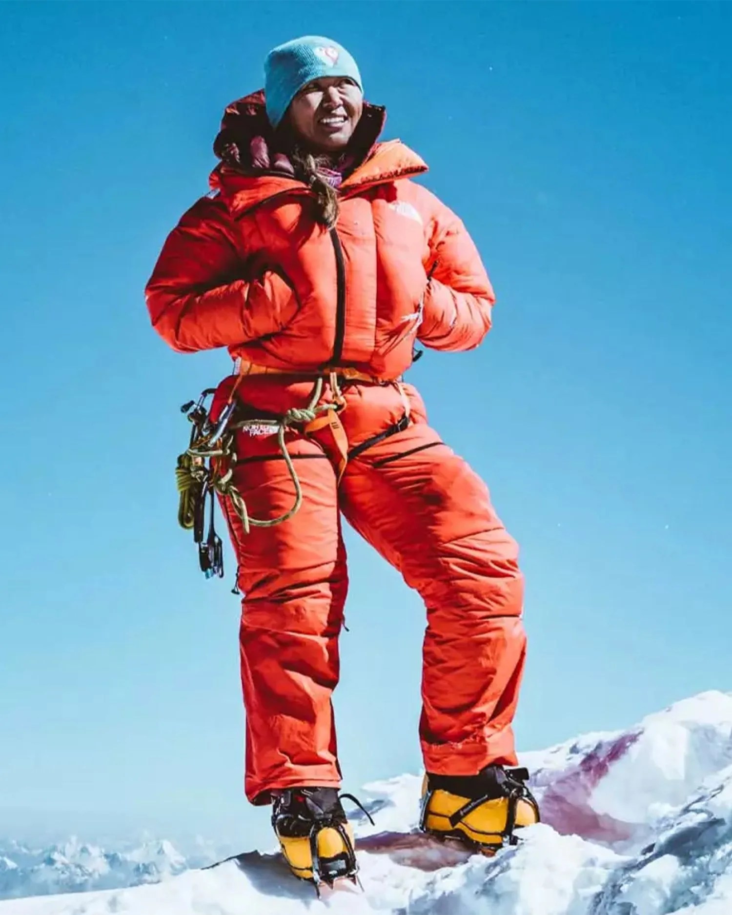 a woman standing on a snowy mountain wearing an orange snowsuit