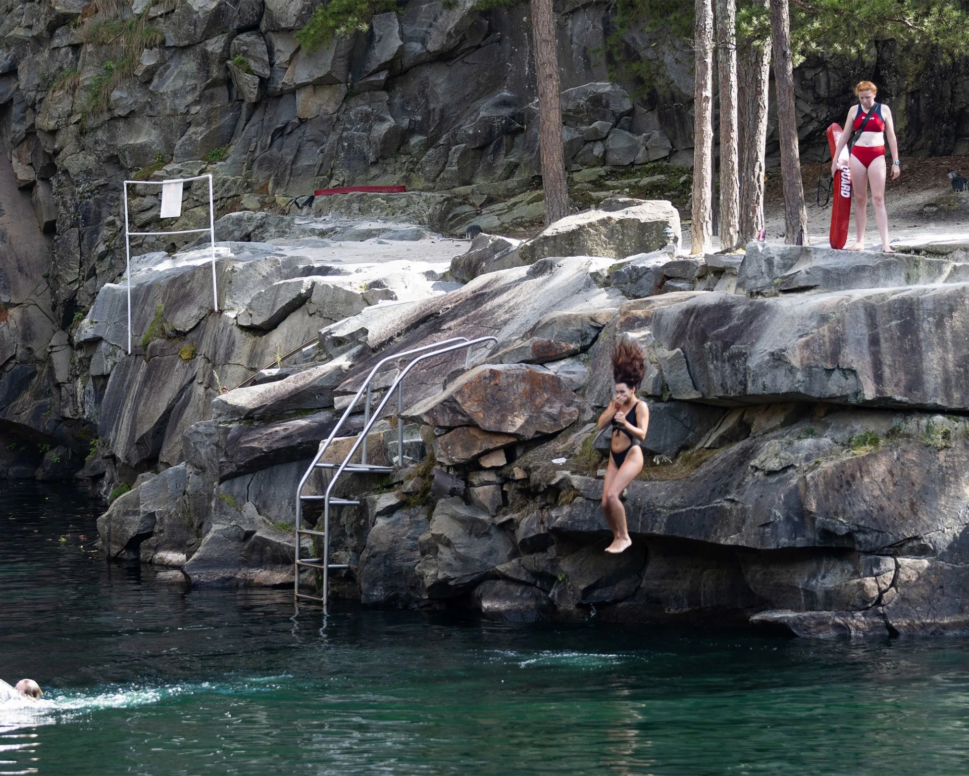 woman jumping into swimming hole being watched by a female lifeguard