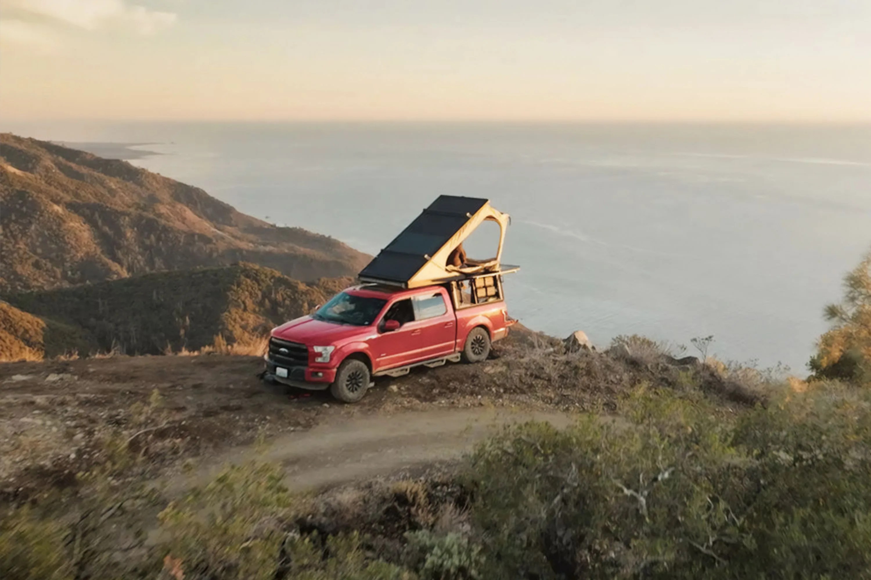 a truck on a mountain with an overlanding tent over looking the ocean