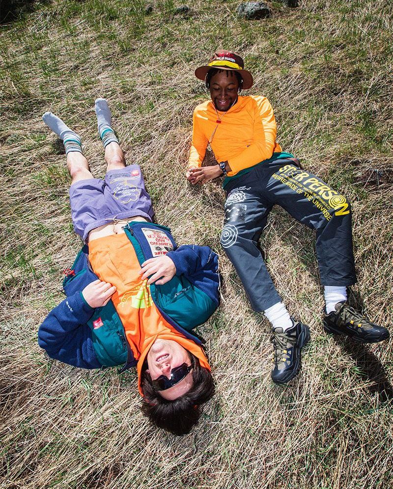 two men wearing the north face x online ceramics collaboration laying down on grassy field