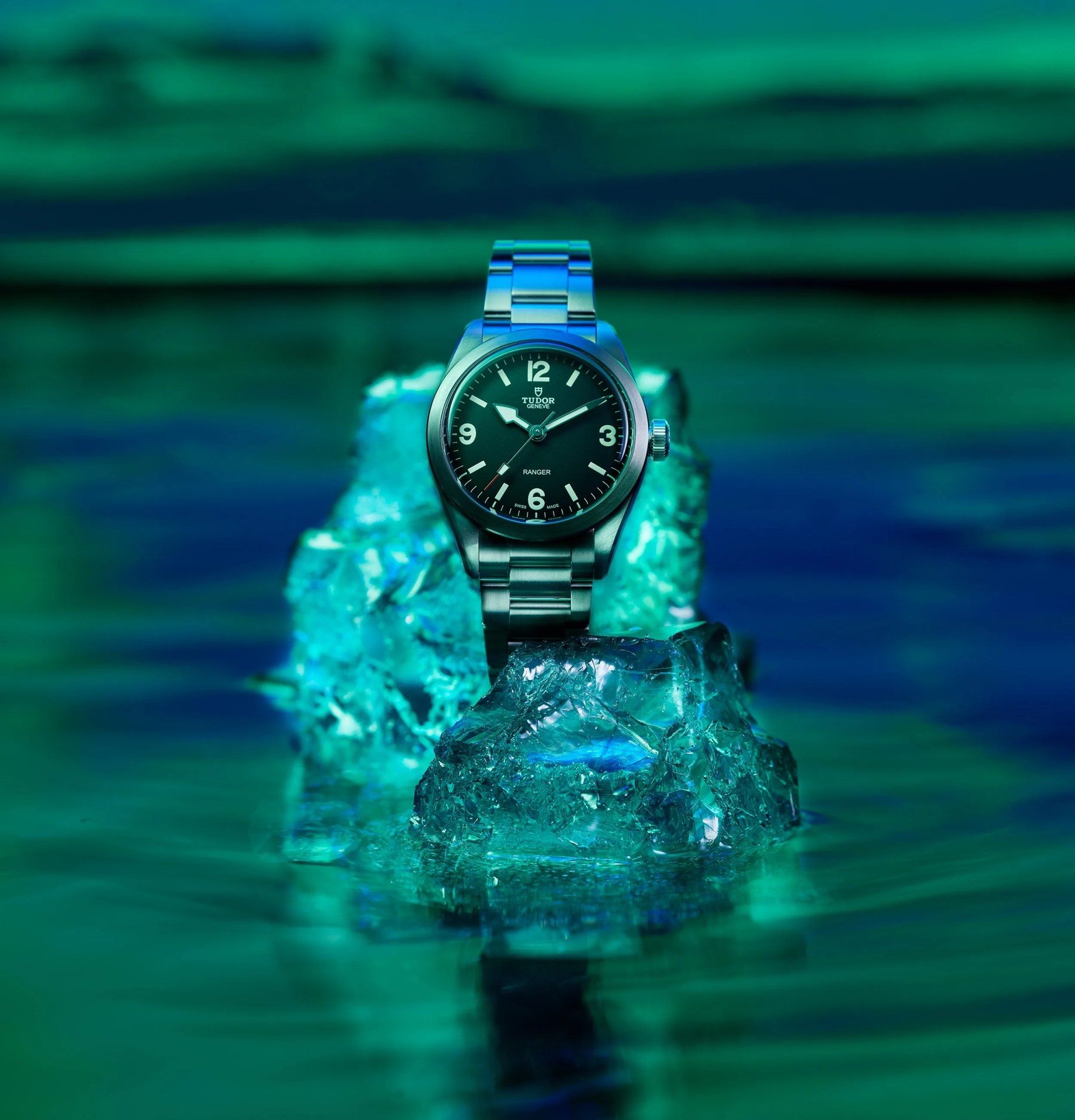 Stainless steel Tudor Ranger wristwatch with black dial on blue-green illuminated ice chunks.
