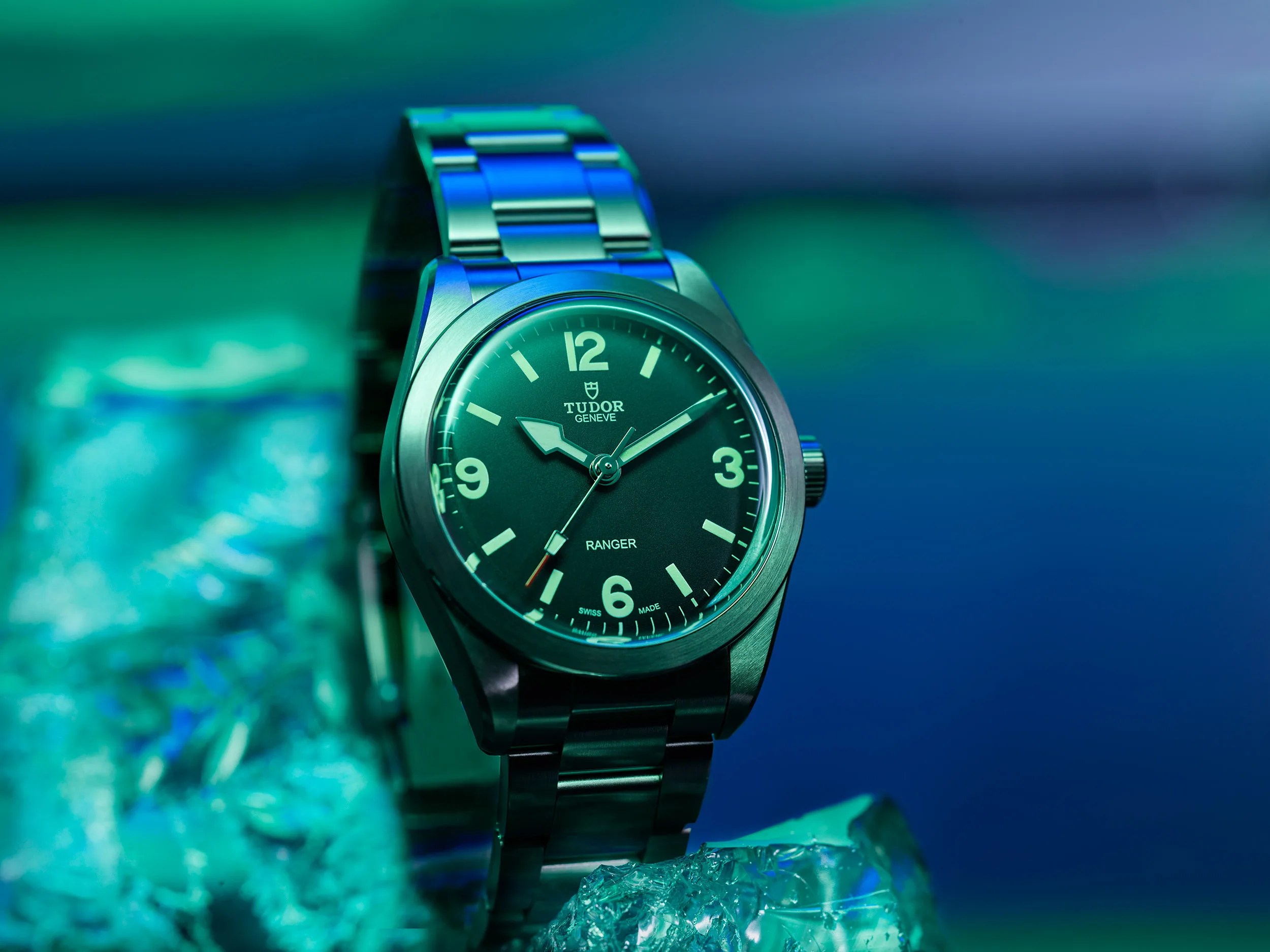 Stainless steel Tudor Ranger wristwatch with black dial and luminous markers on blue-green textured surface.