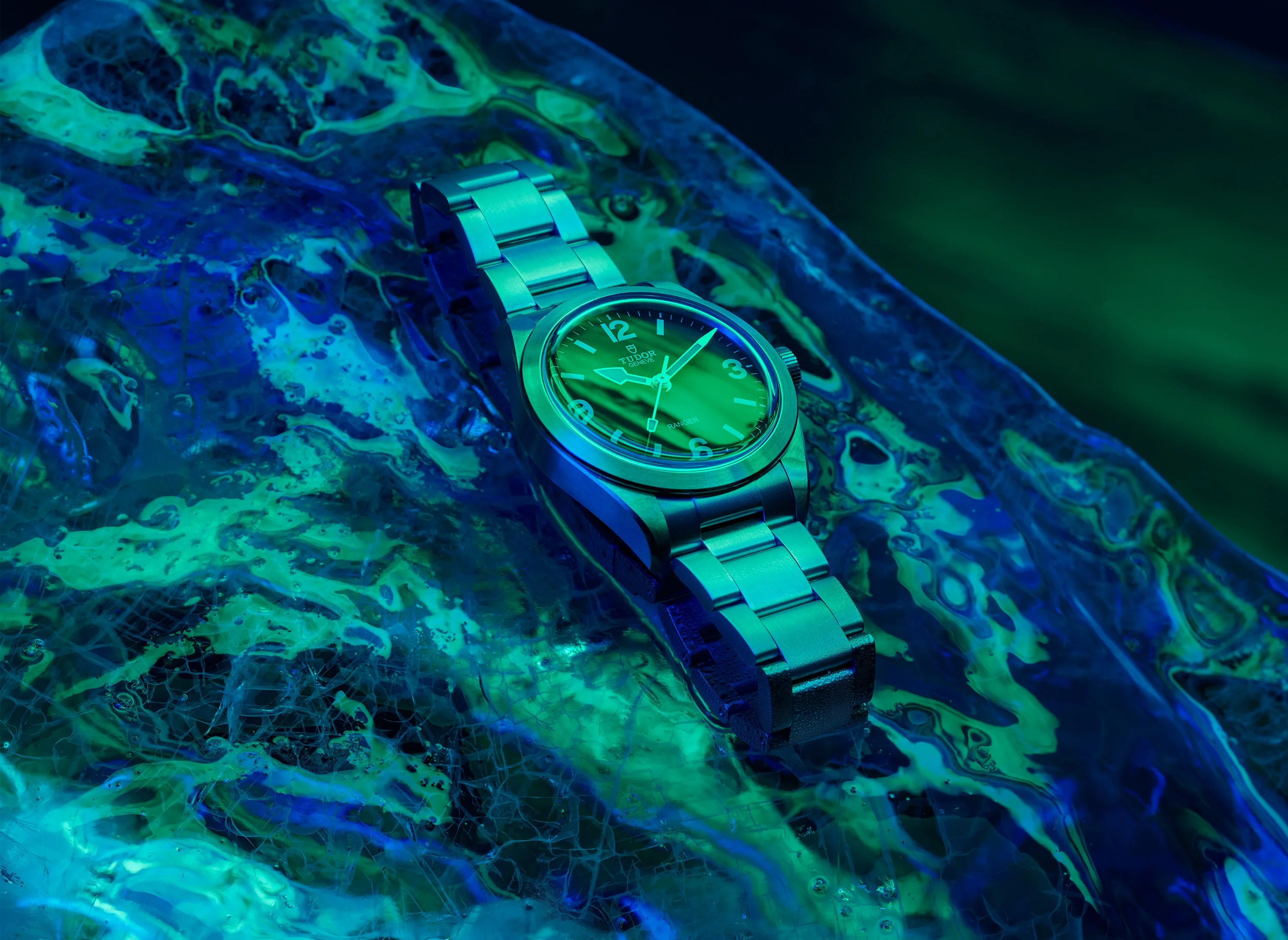 Stainless steel Tudor Ranger wristwatch with black dial on a textured blue-green surface.