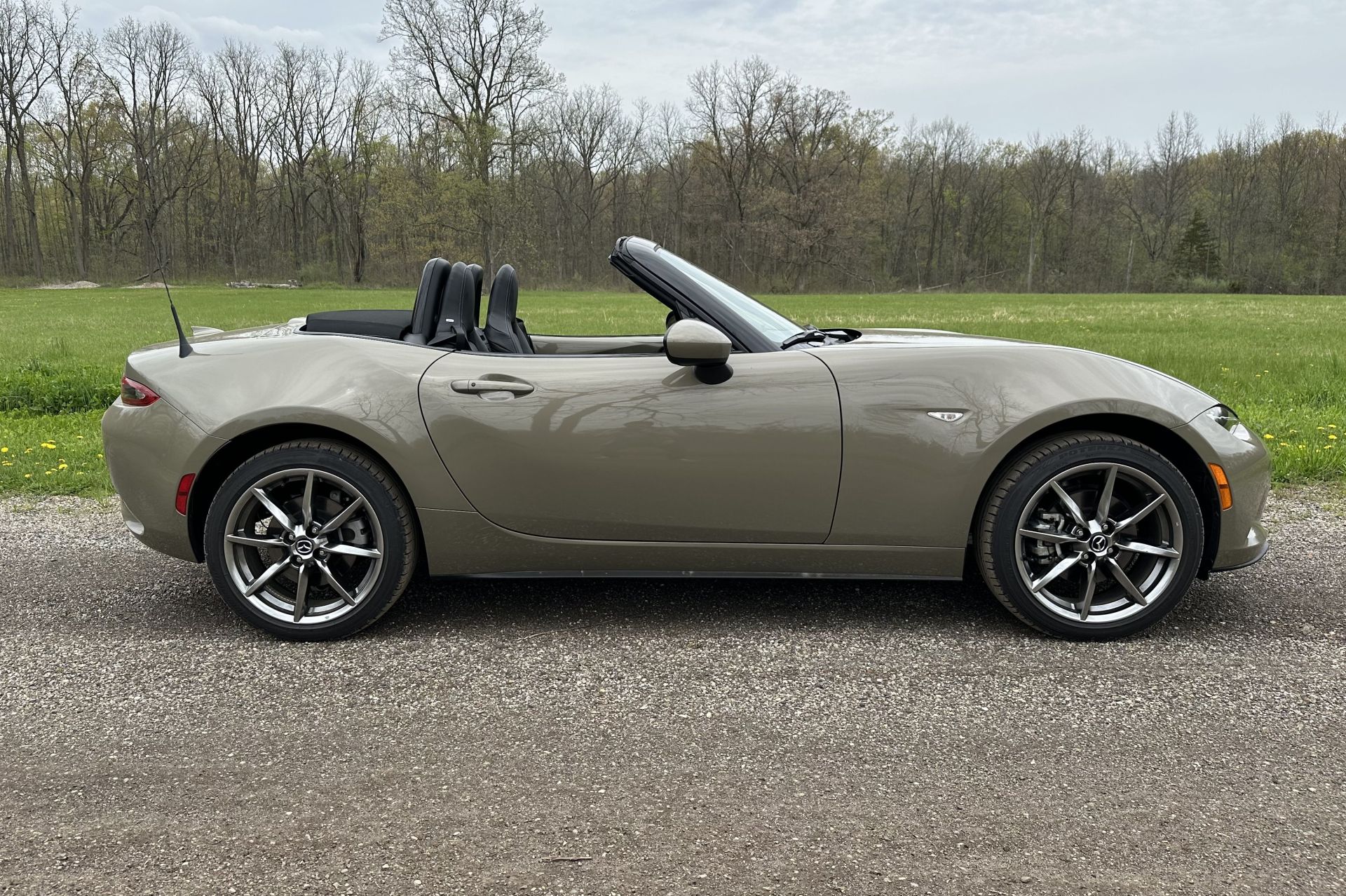 mazda mx5 parked on a dirt road with a field and trees in the background