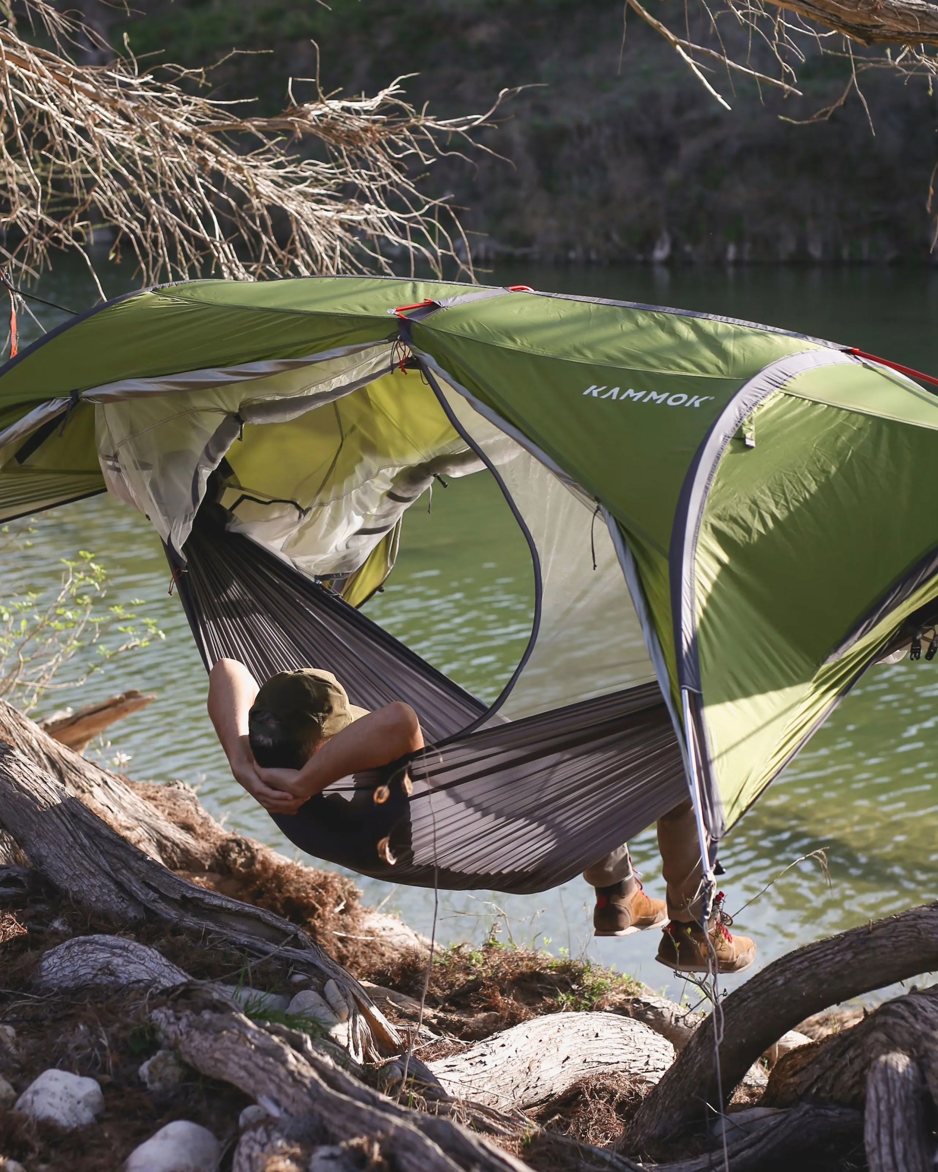 man lounging in kammok sunda 2 hammock tent in front of river