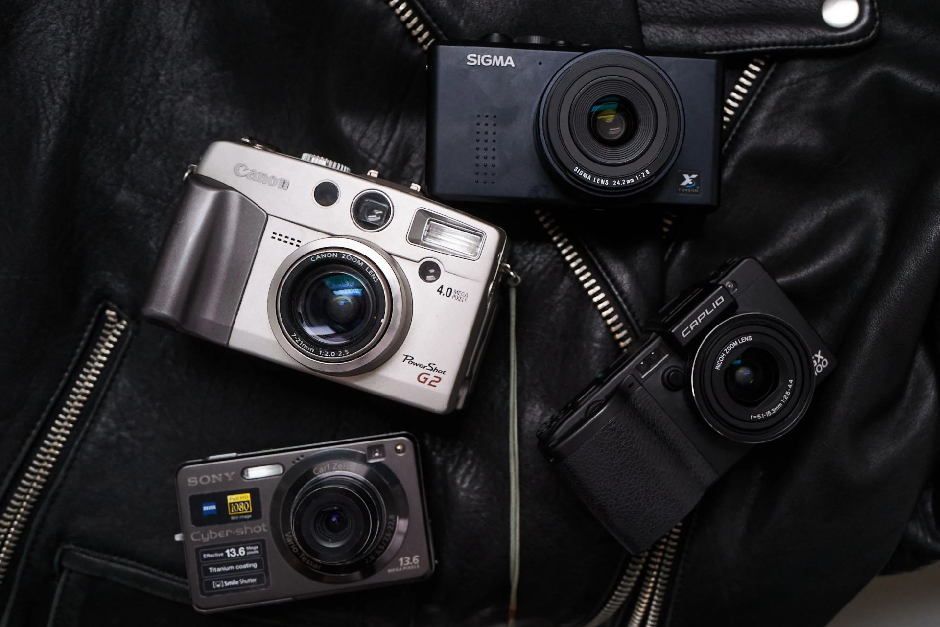 four cameras laying on a black leather jacket