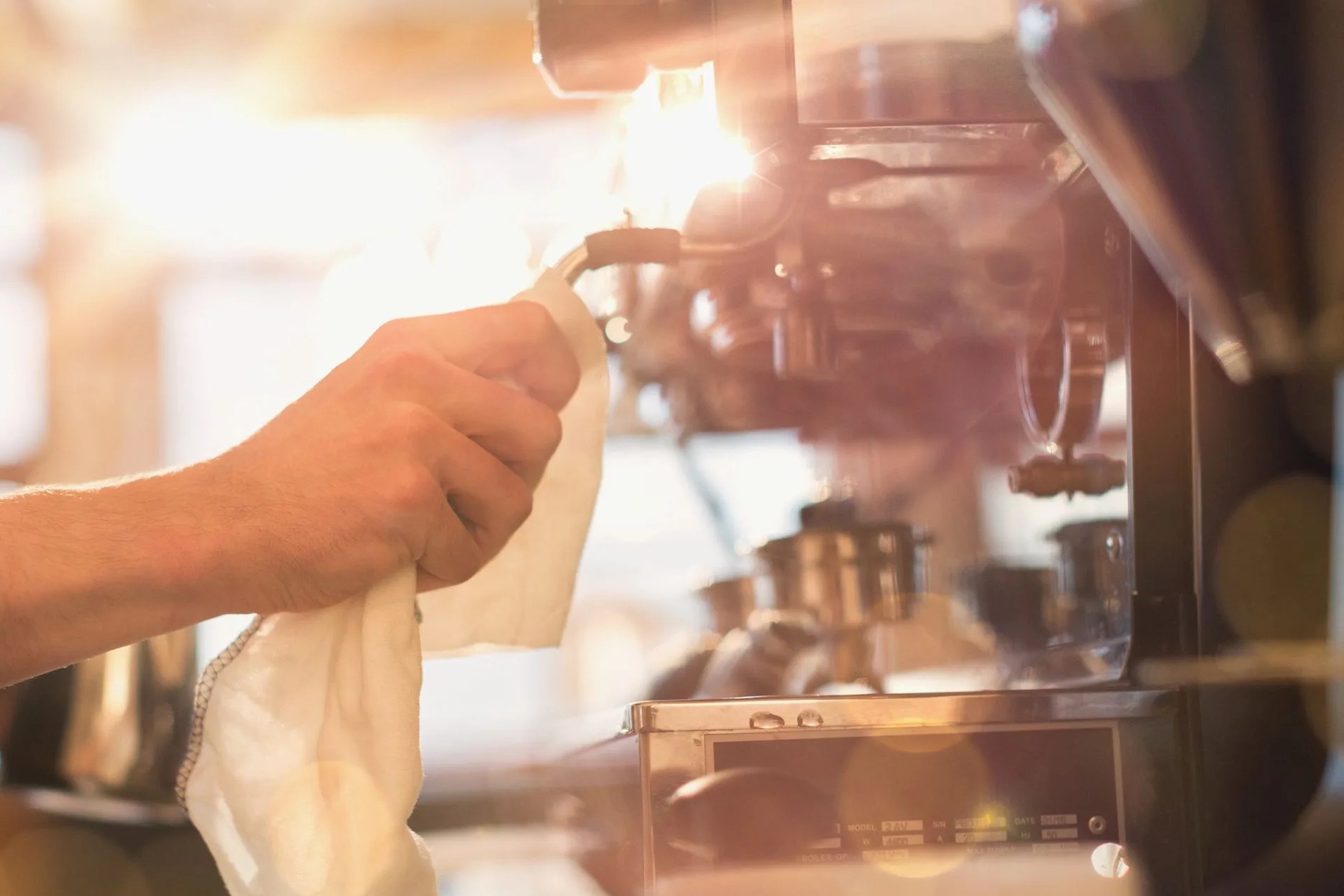 close up barista wiping down espresso machine milk frother with rag in cafe