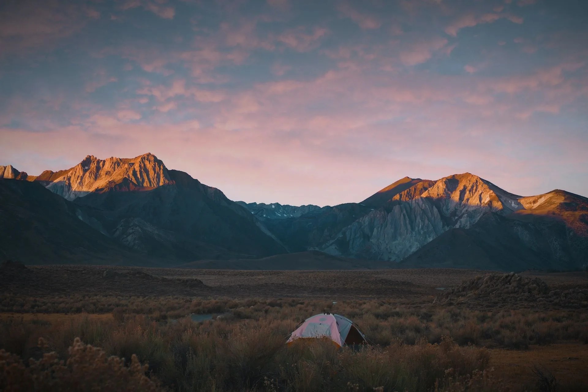 camping in field by mountains as sun rises