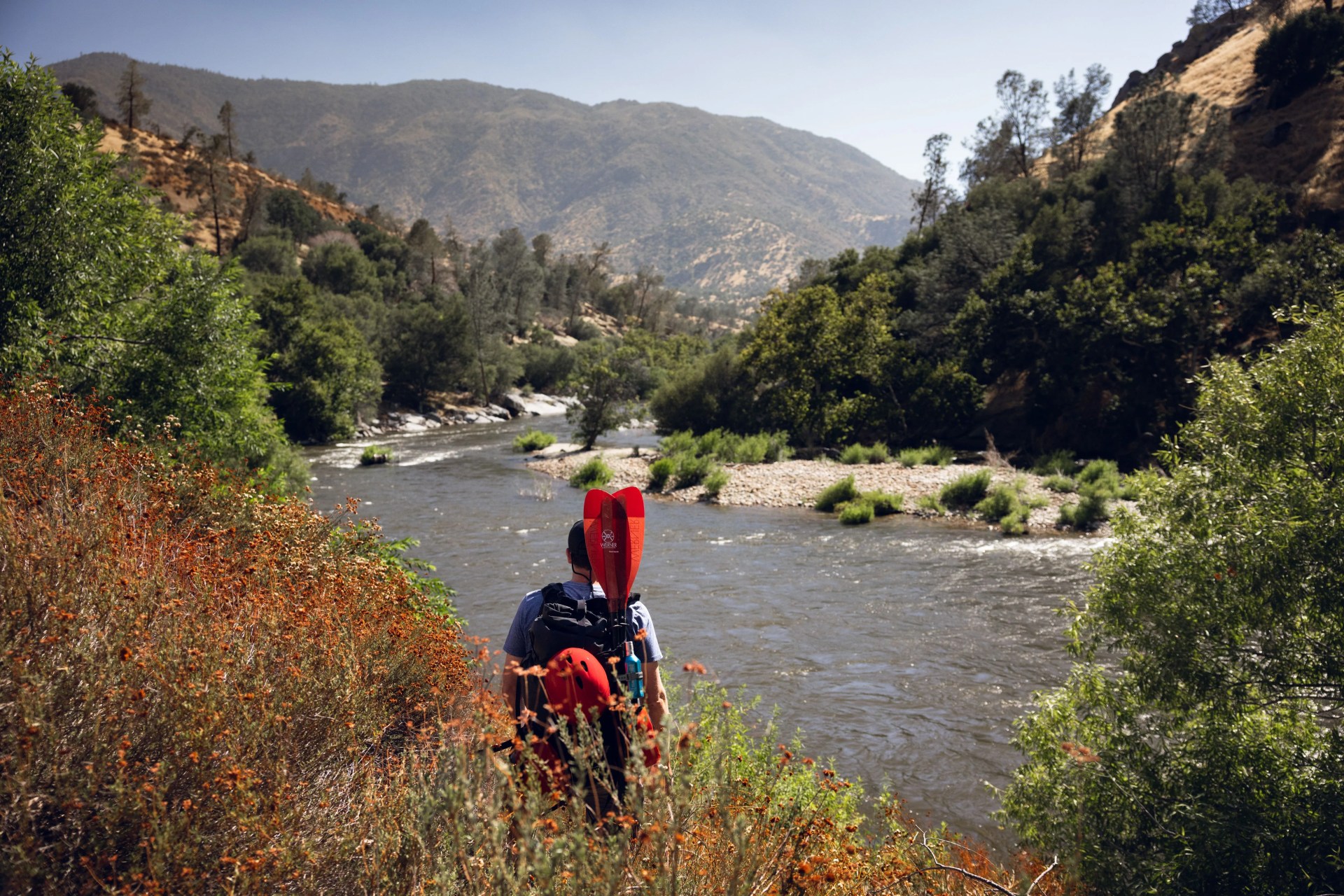 man looking at river carrying gear with tincup whiskey