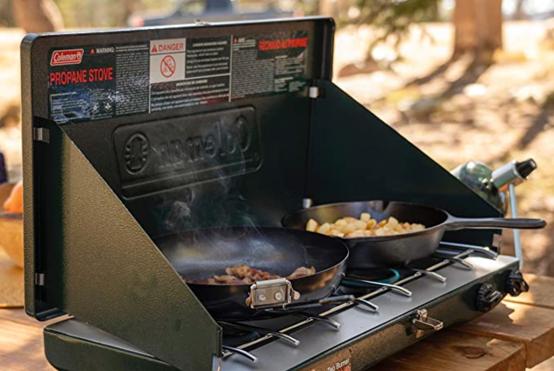 a camping stove with two pans cooking food on a picnic table