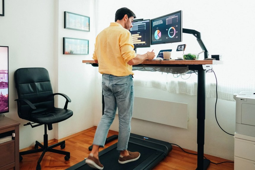 man working from home at standing desk is walking on under desk treadmill