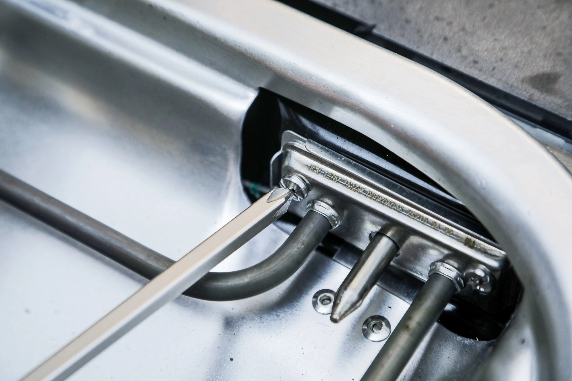 electric grill coil being removed with a screwdriver