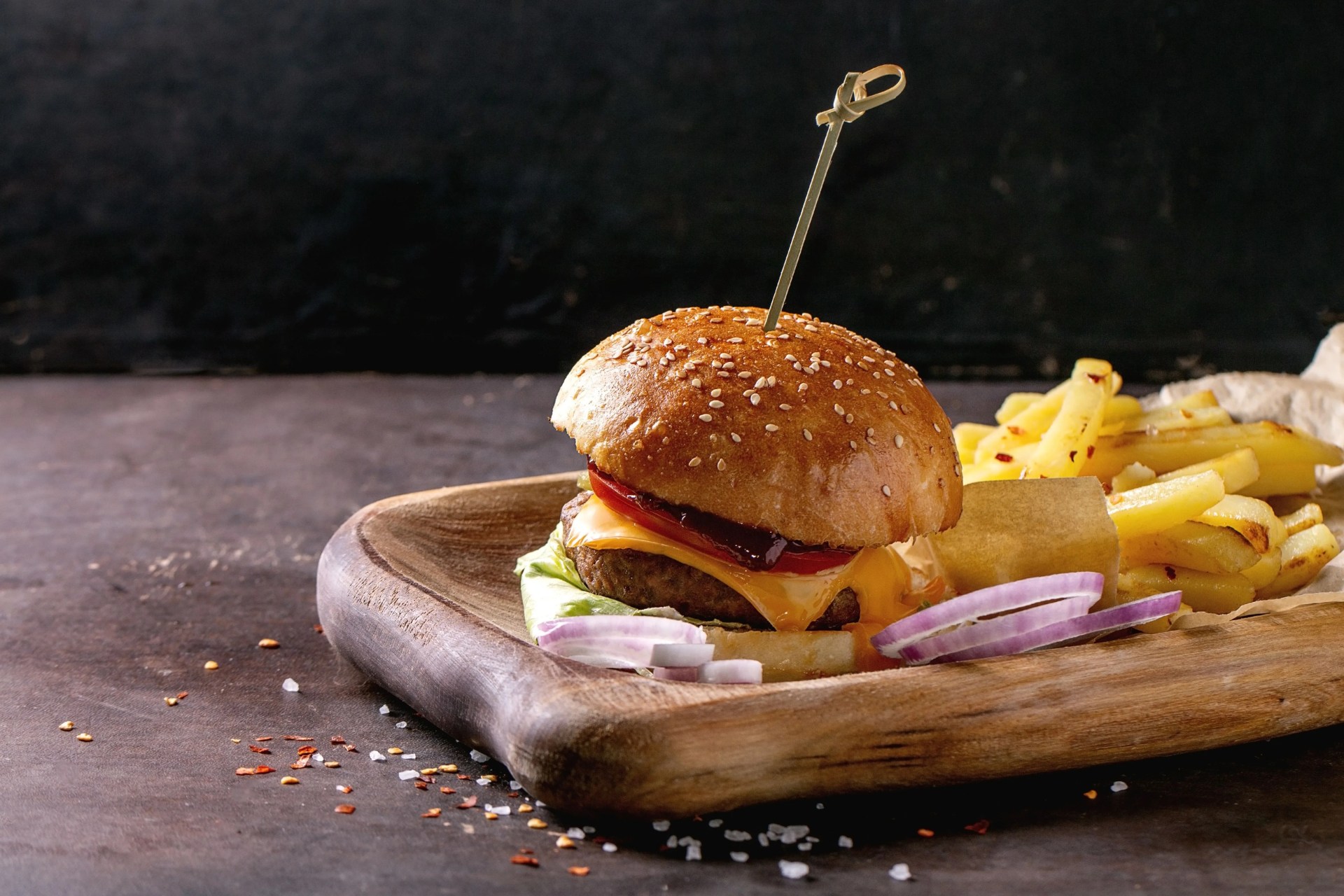 wooden plate with fresh homemade burger and grilled potatoes over dark background