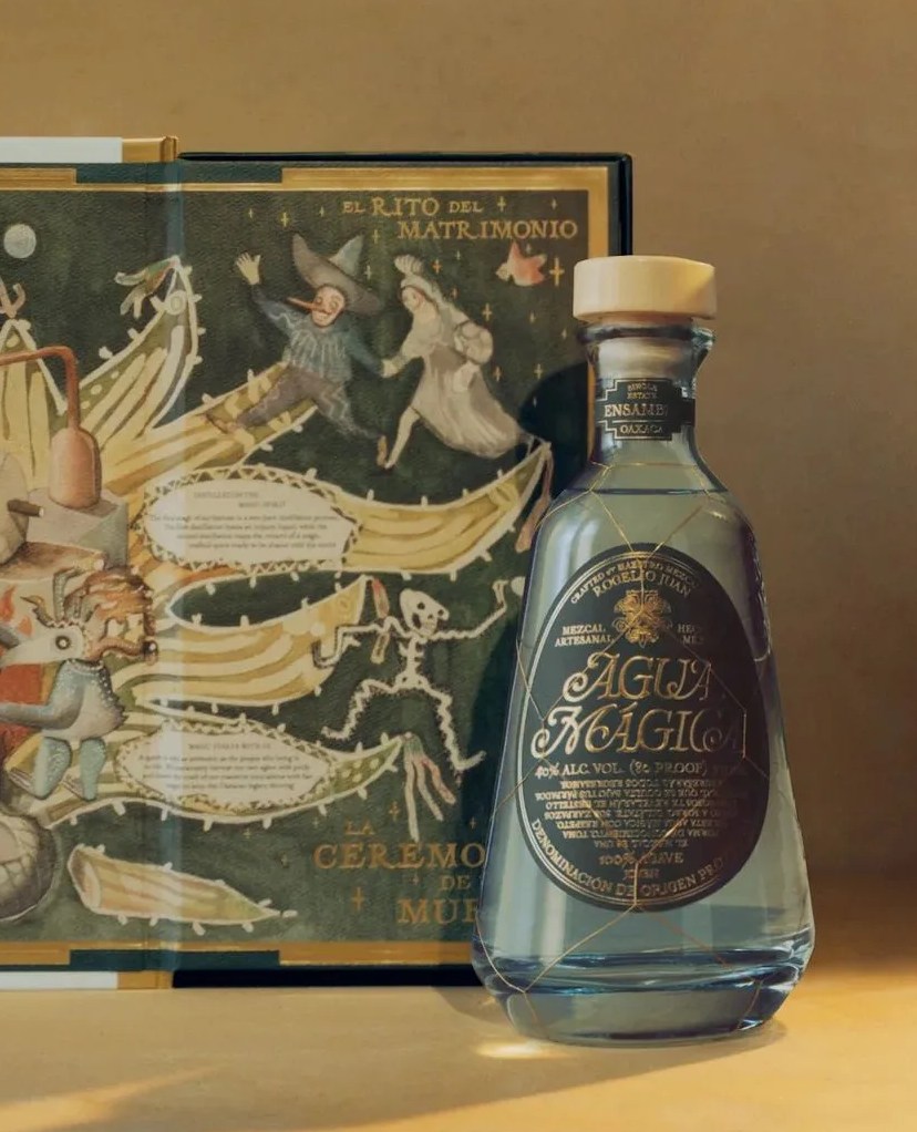 a bottle of alcohol next to a painted gift box from agua mágica