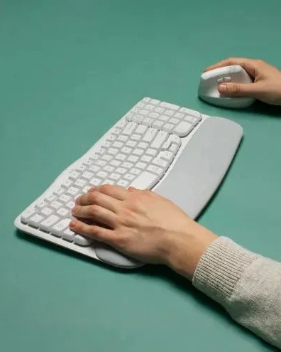 a person typing on a logitech white keyboard with wave keys