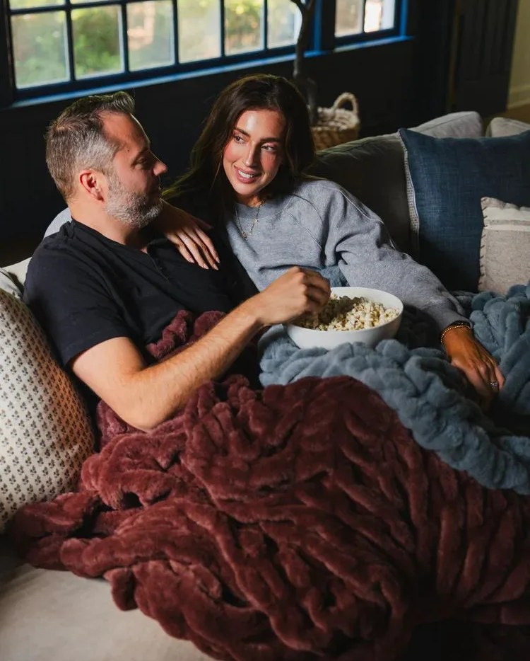 a man and woman sitting on a couch eating popcorn using lola blankets
