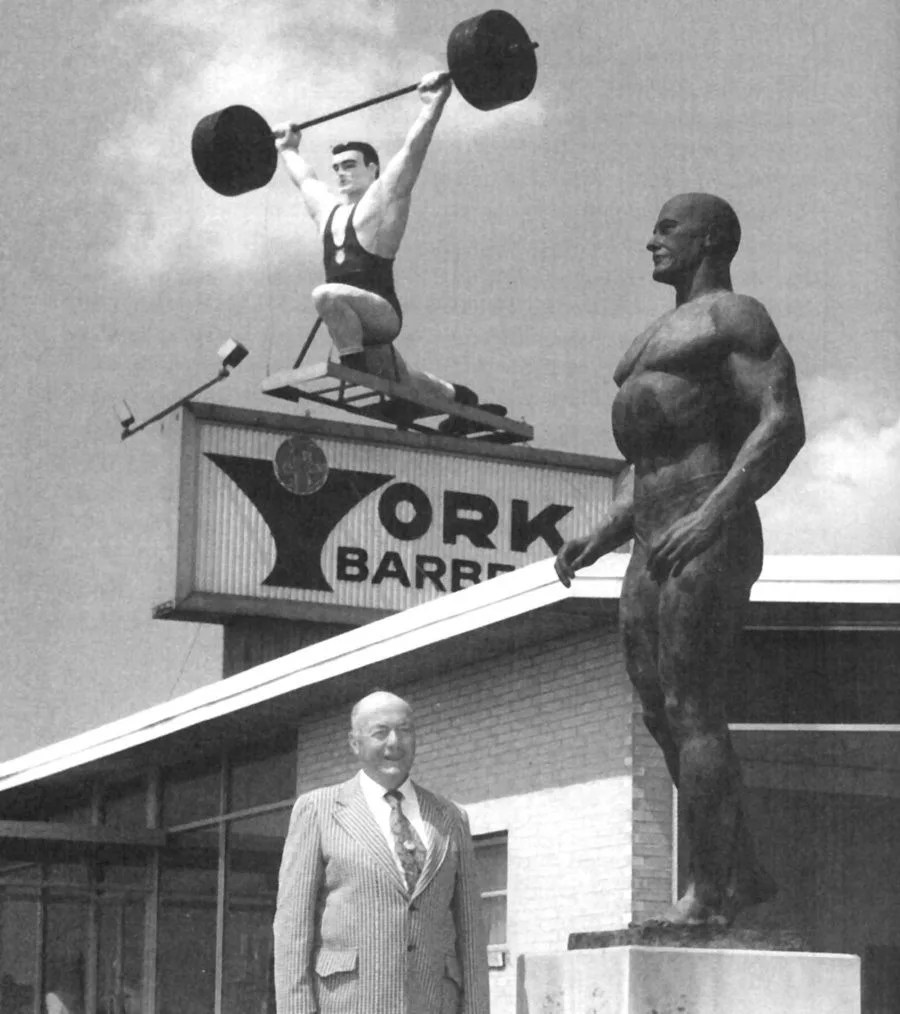 a black and white photo of a man standing in front of york barbell company