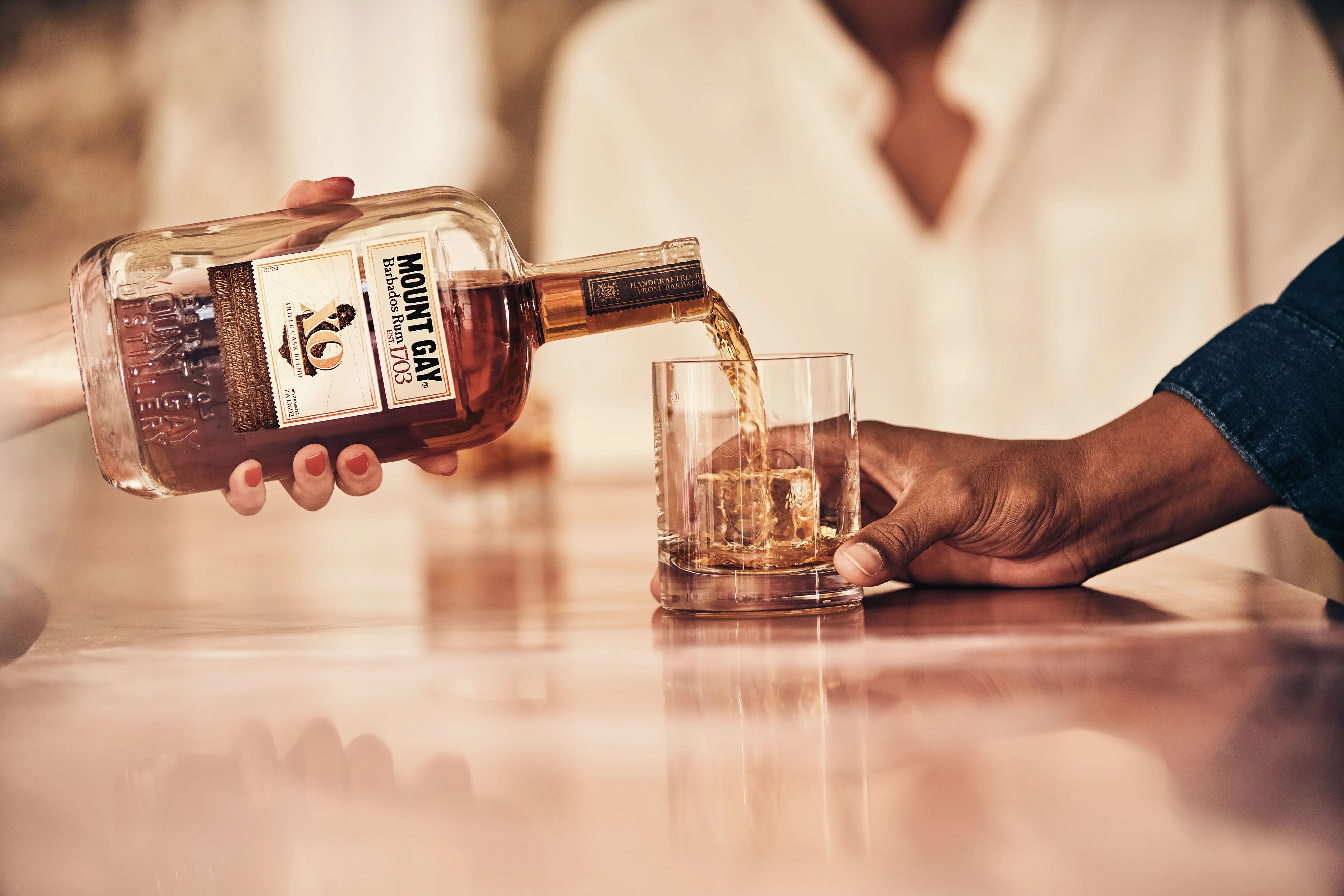a person pouring mount gay rum xo into a glass for another person