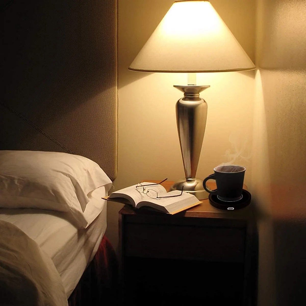 a lamp and a book on a table with a cup of coffee warmed by a smart coffee warmer