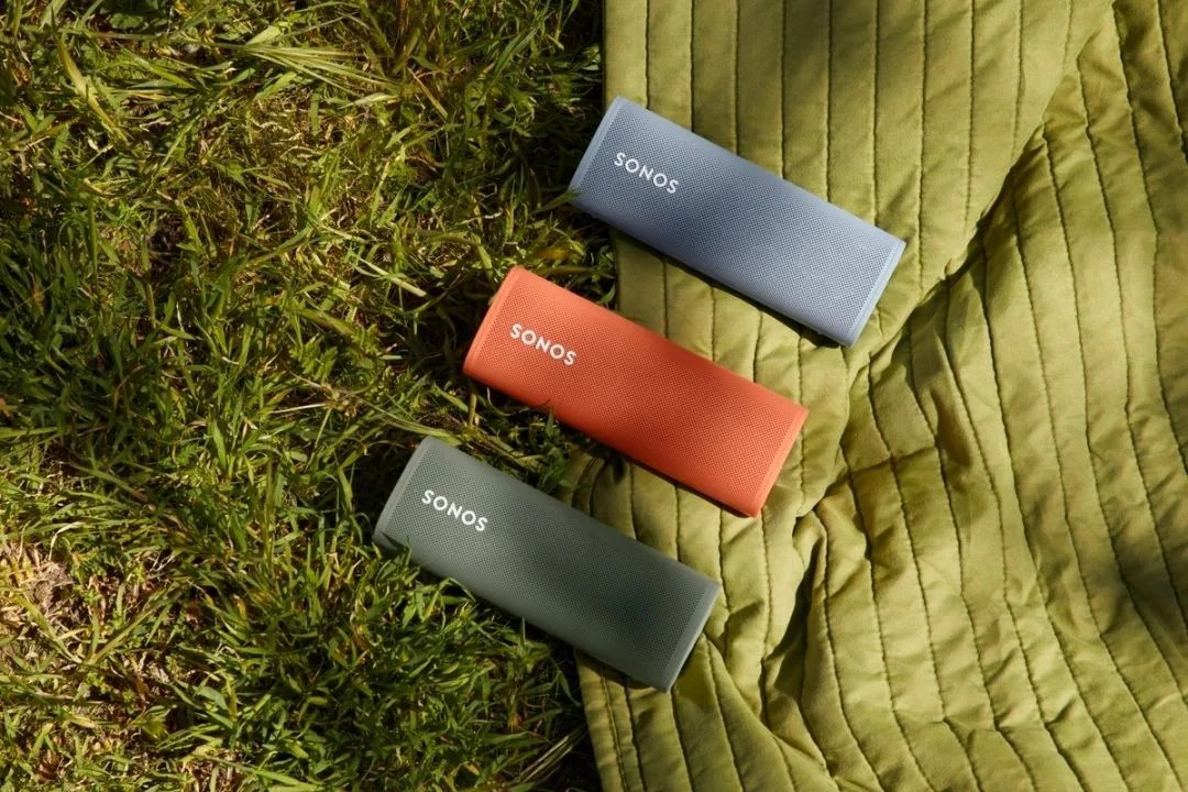 a trio of sonos roam speakers laying on the grassy floor and blanket