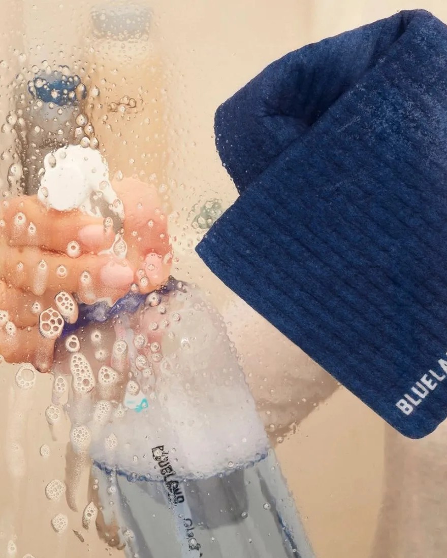a person cleaning a glass shower while holding a blueland cloud cloth