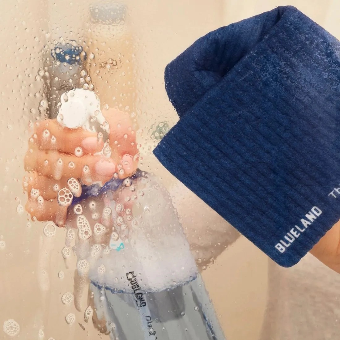 a person cleaning a glass shower while holding a blueland cloud cloth