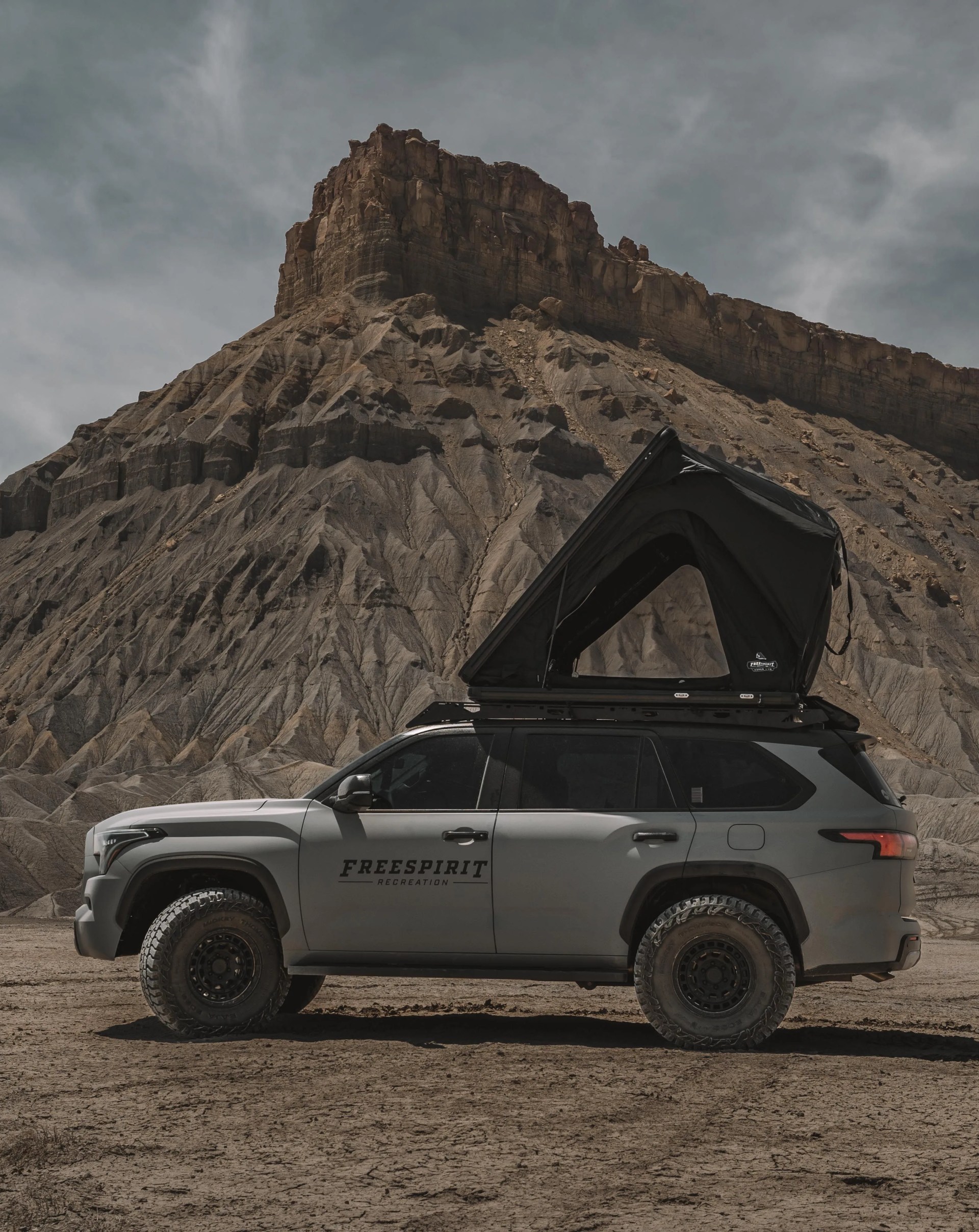 a truck with a free spirit recreation tent parked in front of a large rock formation