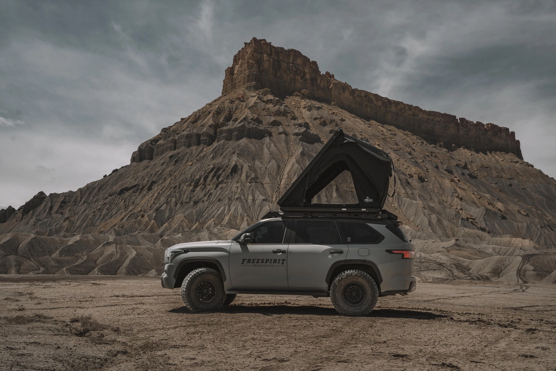 a truck with a free spirit recreation tent parked in front of a large rock formation