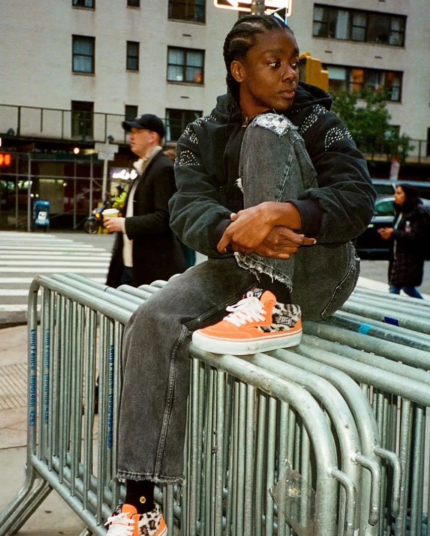 a man sitting on a railing wearing new supreme x vans sneakers