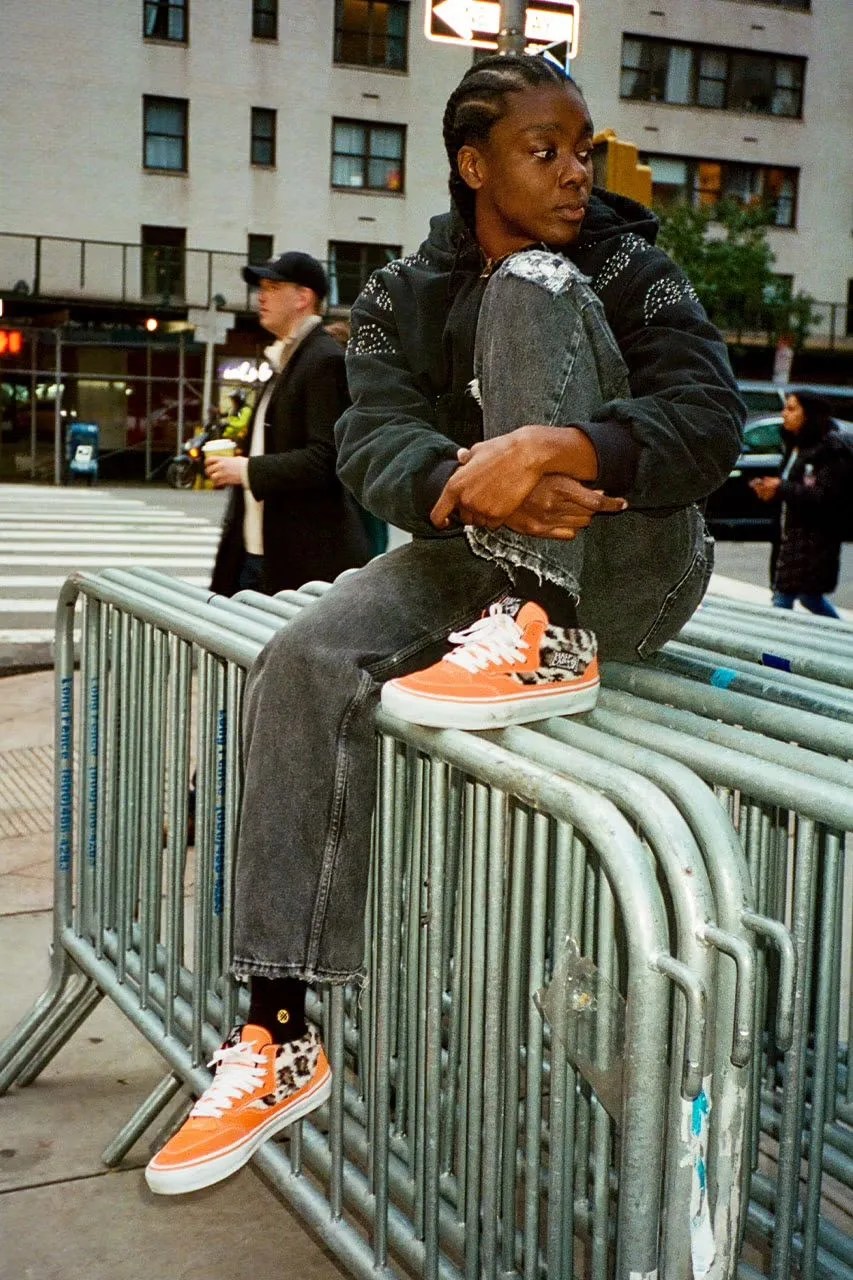a man sitting on a railing wearing new supreme x vans sneakers