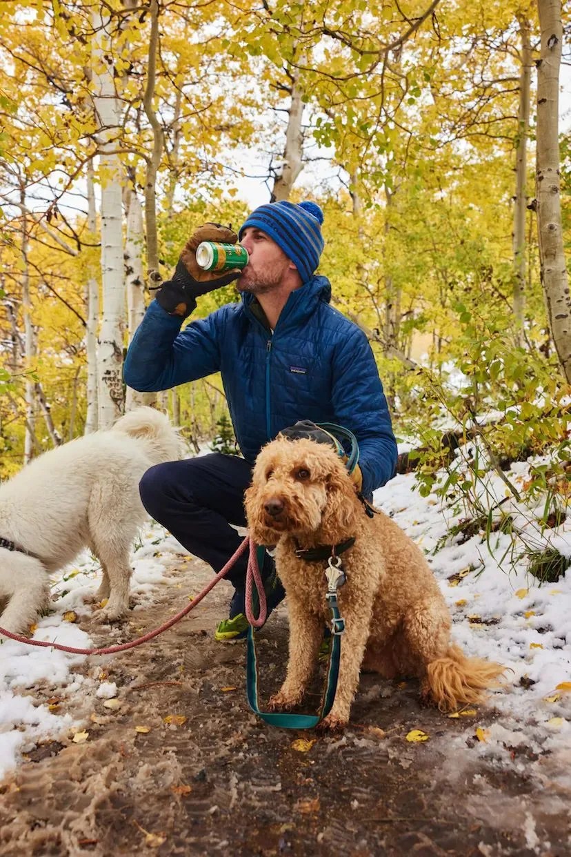 a person drinking a can of sierra nevada beer crouched by a dog
