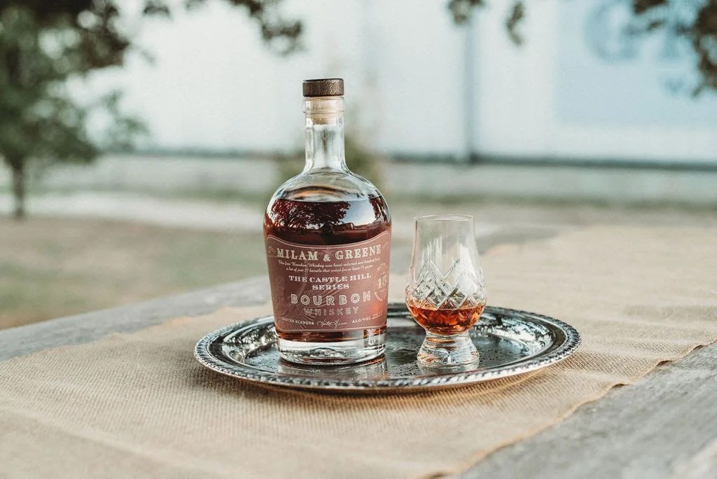a bottle of milam and greene whiskey and a glass of whiskey on a table