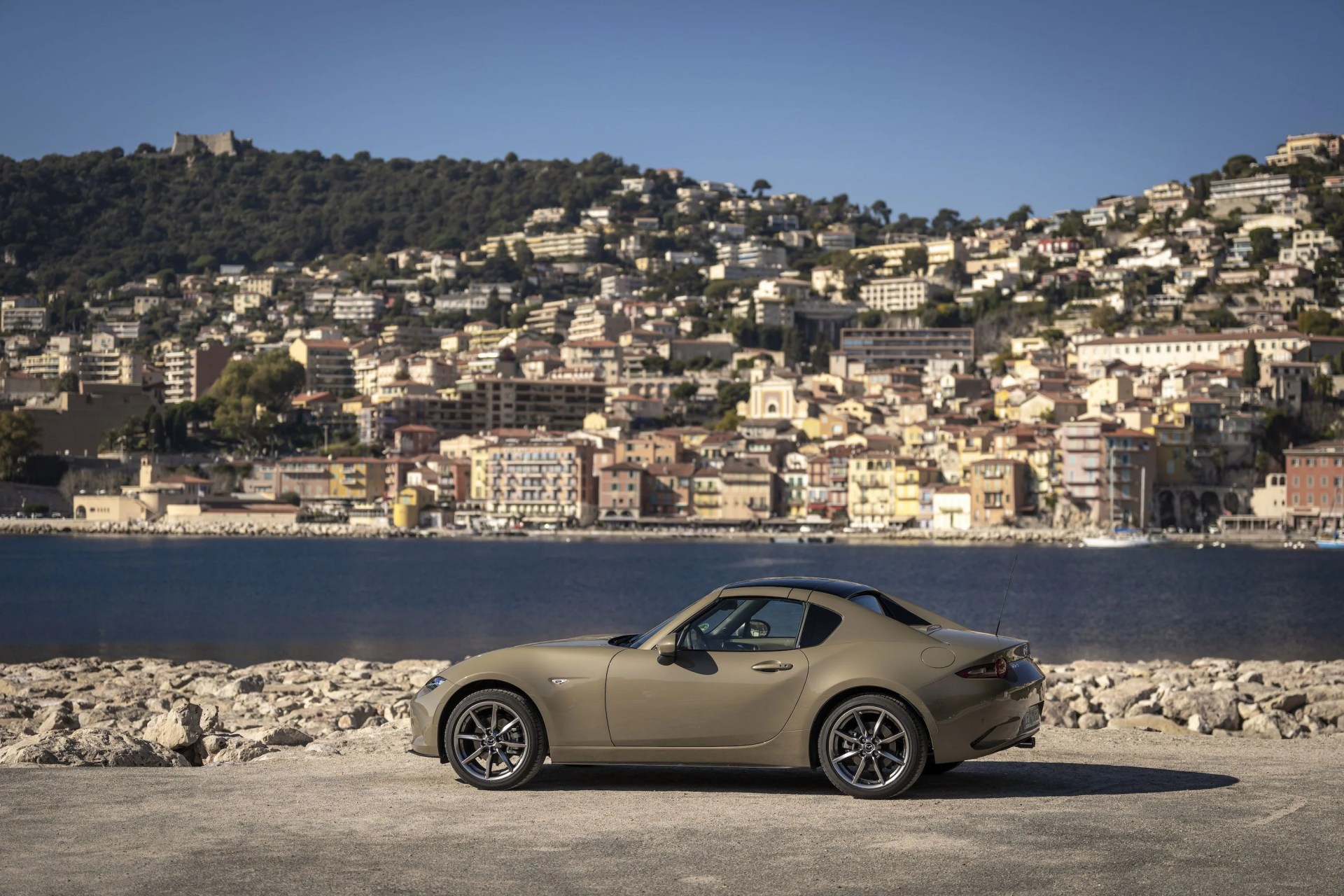 a car parked on a road by a body of water with a city in the background