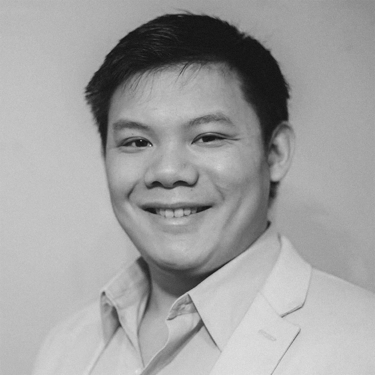 A black and white portrait of a smiling man with short, dark hair. He is wearing a light-colored blazer over a collared shirt. The background is plain and unobtrusive.